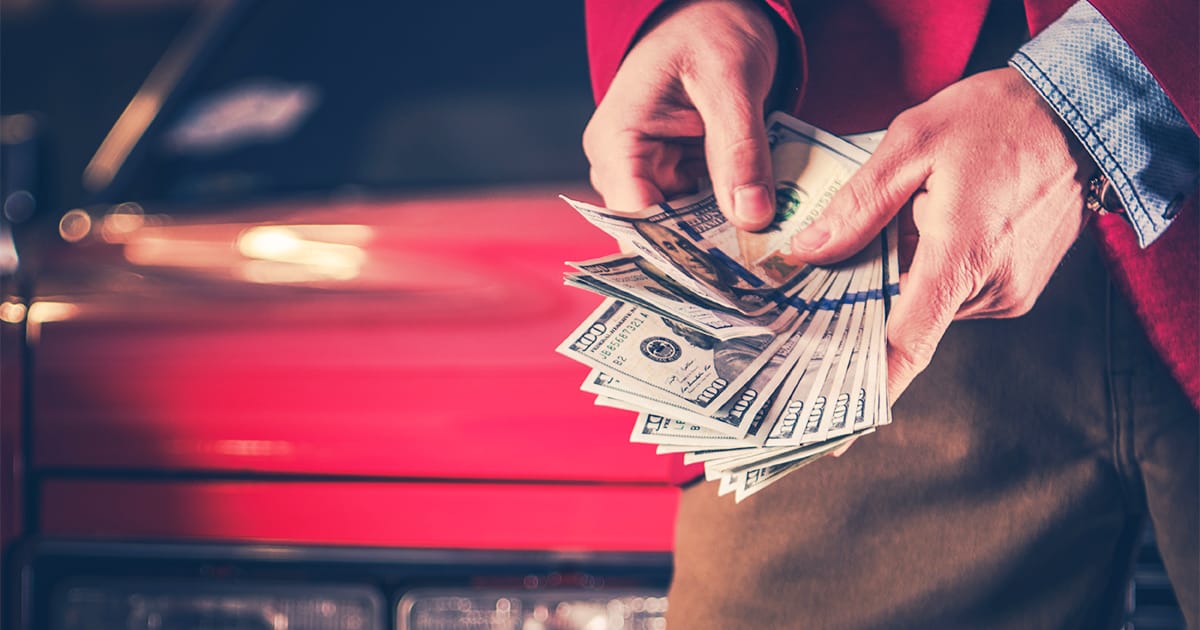 Man counting american money in front of a red vintage car