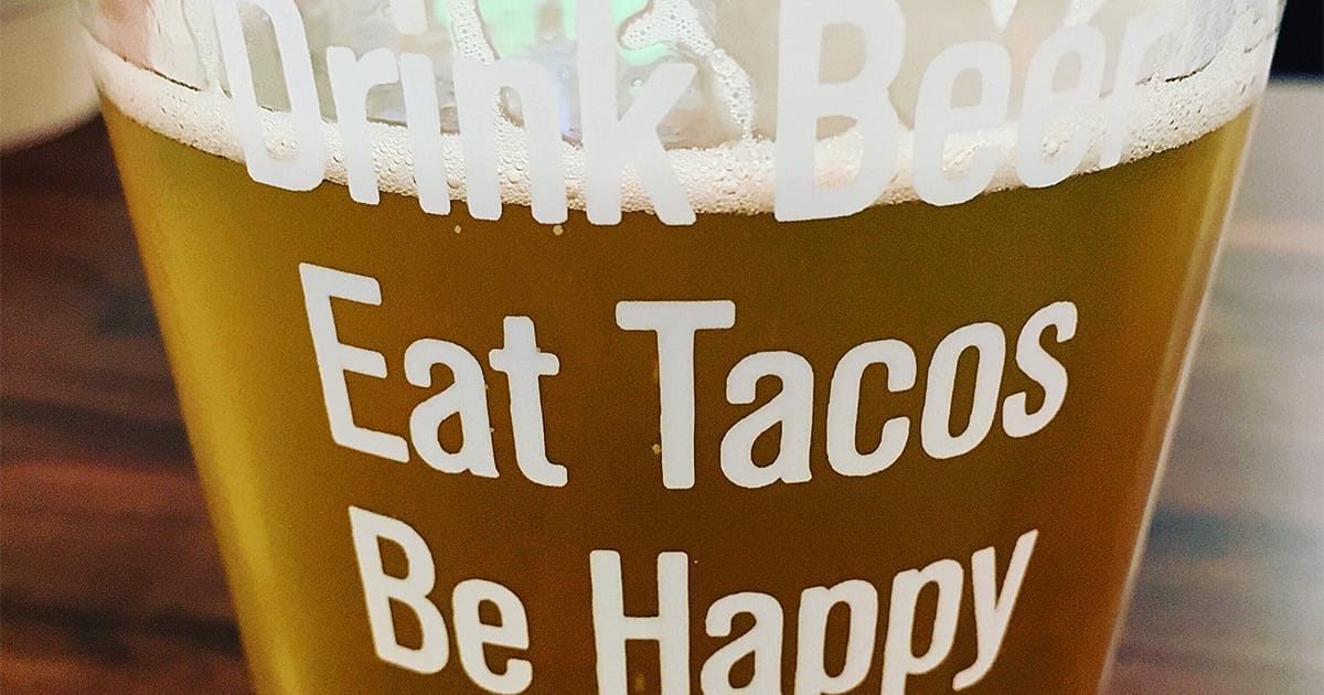 beer in a glass that has print on it saying 'Drink beer. eat tacos. be happy. '