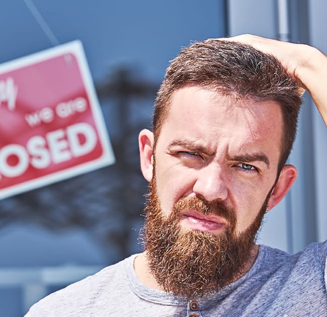 A man in distress standing in front of a closed business sign